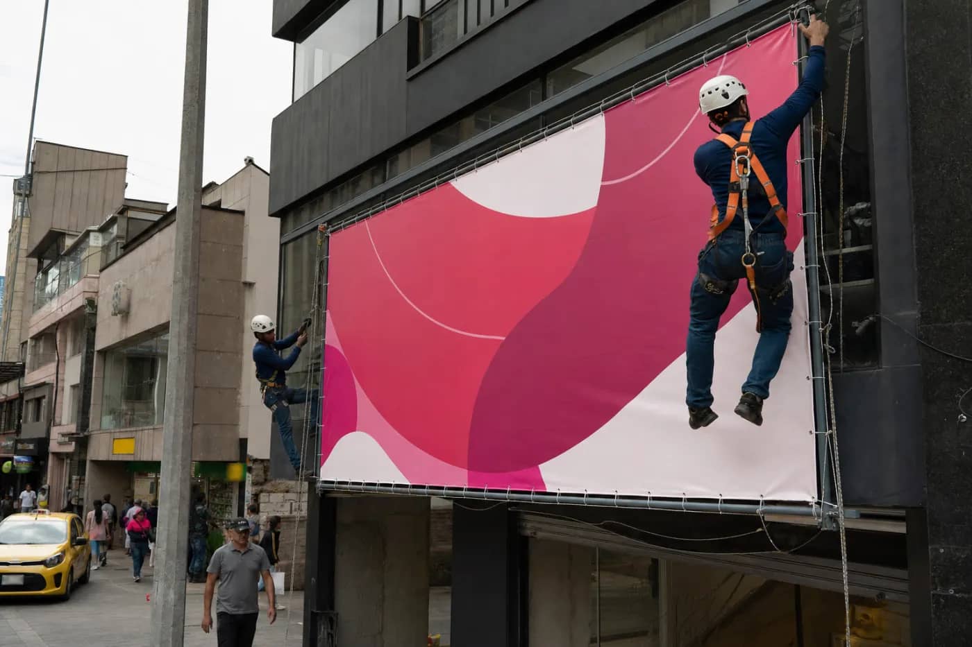Instaladores con arnés tensando la lona de un bastidor publicitario sobre la fachada de un local comercial