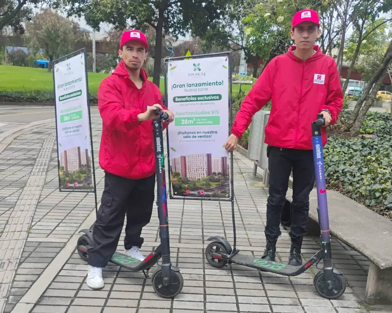 Dos promotores de Bagu Medios con scooter valla: patinetas eléctricas con valla vertical de un proyecto inmobiliario